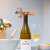 White wine bottle with a humorous bottle stopper shaped like a man with the dick as the wine stopper, set against a casual dining background.