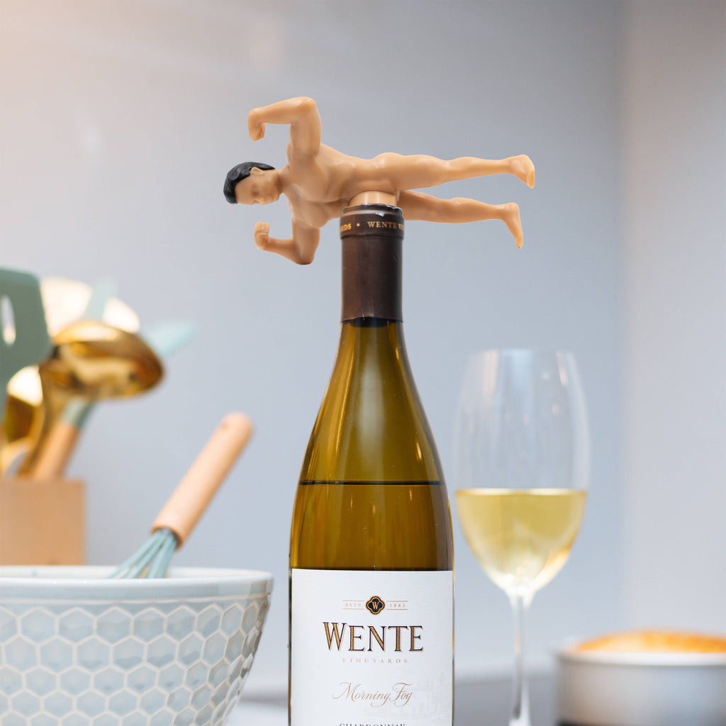 White wine bottle with a humorous bottle stopper shaped like a man with the dick as the wine stopper, set against a casual dining background.