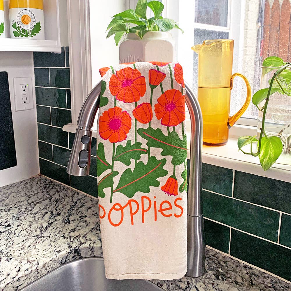 Kitchen towel with floral poppy design hanging over a faucet in a kitchen.