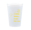 Frost flex clear 12oz cup with a bee design is shown against a white background. The cup features an image of a bee and text in yellow font that reads "A little honey is on the way" - perfect for bee-themed baby shower bar set ups. 