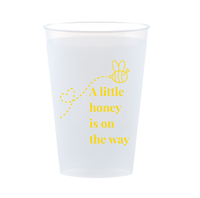 Frost flex clear 12oz cup with a bee design is shown against a white background. The cup features an image of a bee and text in yellow font that reads "A little honey is on the way" - perfect for bee-themed baby shower bar set ups. 