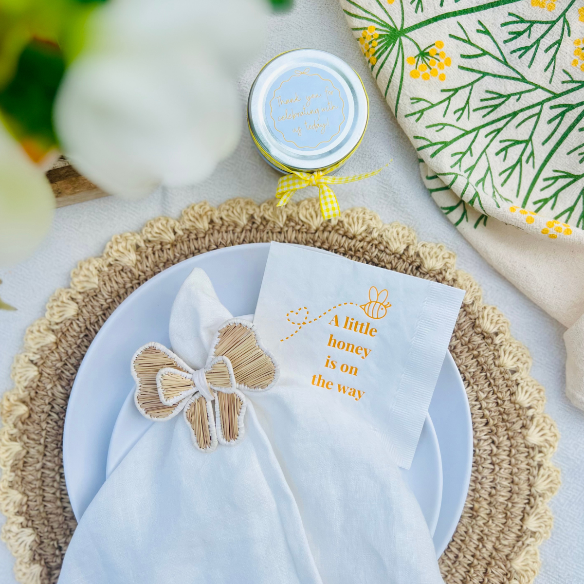 Baby shower-themed napkin with a bee and text that reads "A Little Honey Is On The Way" is shown from above on a plate. 