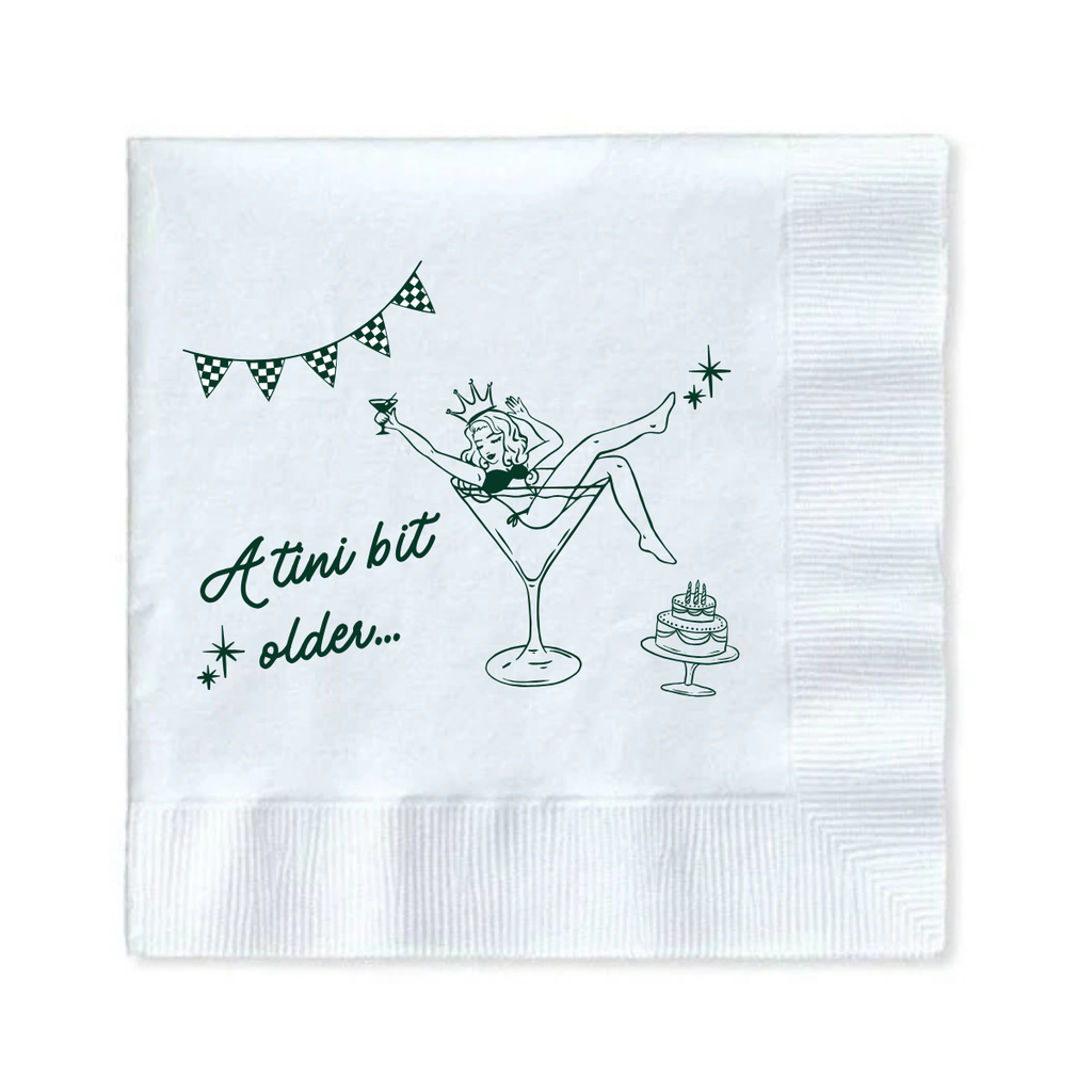 White paper cocktail napkin with a girl in a martini glass and text that reads "A Tini Bit Older" for martini themed birthday parties and celebrations is shown against a white background