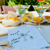 Two martini glasses with chamomile garnishes on a tablecloth with a cocktail napkin featuring text and graphics.