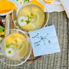 Two chamomile lemon martinis beside a white paper cocktail napkin that features a design of a woman in a martini glass and text that reads "A Tini Bit Older" for martini -themed birthday parties.