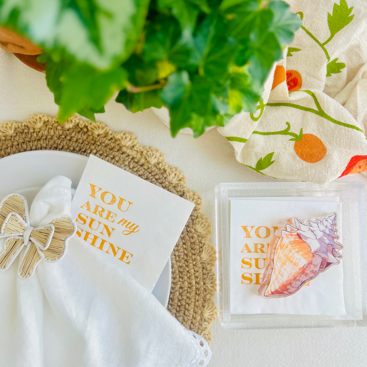 Acrylic shell napkin weight is shown on white paper napkin rings that have text that reads "you are my sunshine."