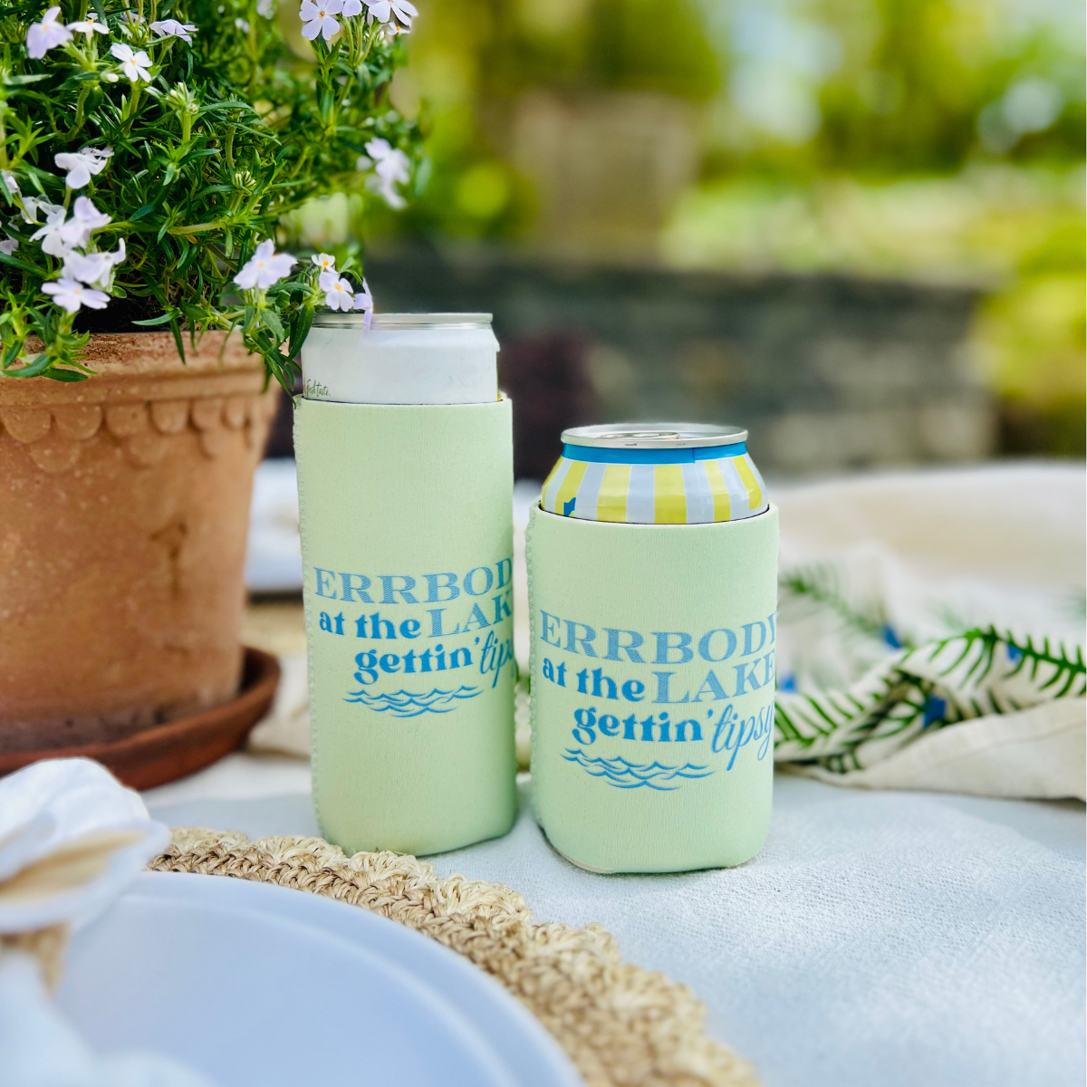Two green can coolers with text on a table outdoors.