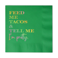 Green paper napkin with holographic gold text that reads 'Feed Me Tacos & Tell Me I'm Pretty' is shown on a white background