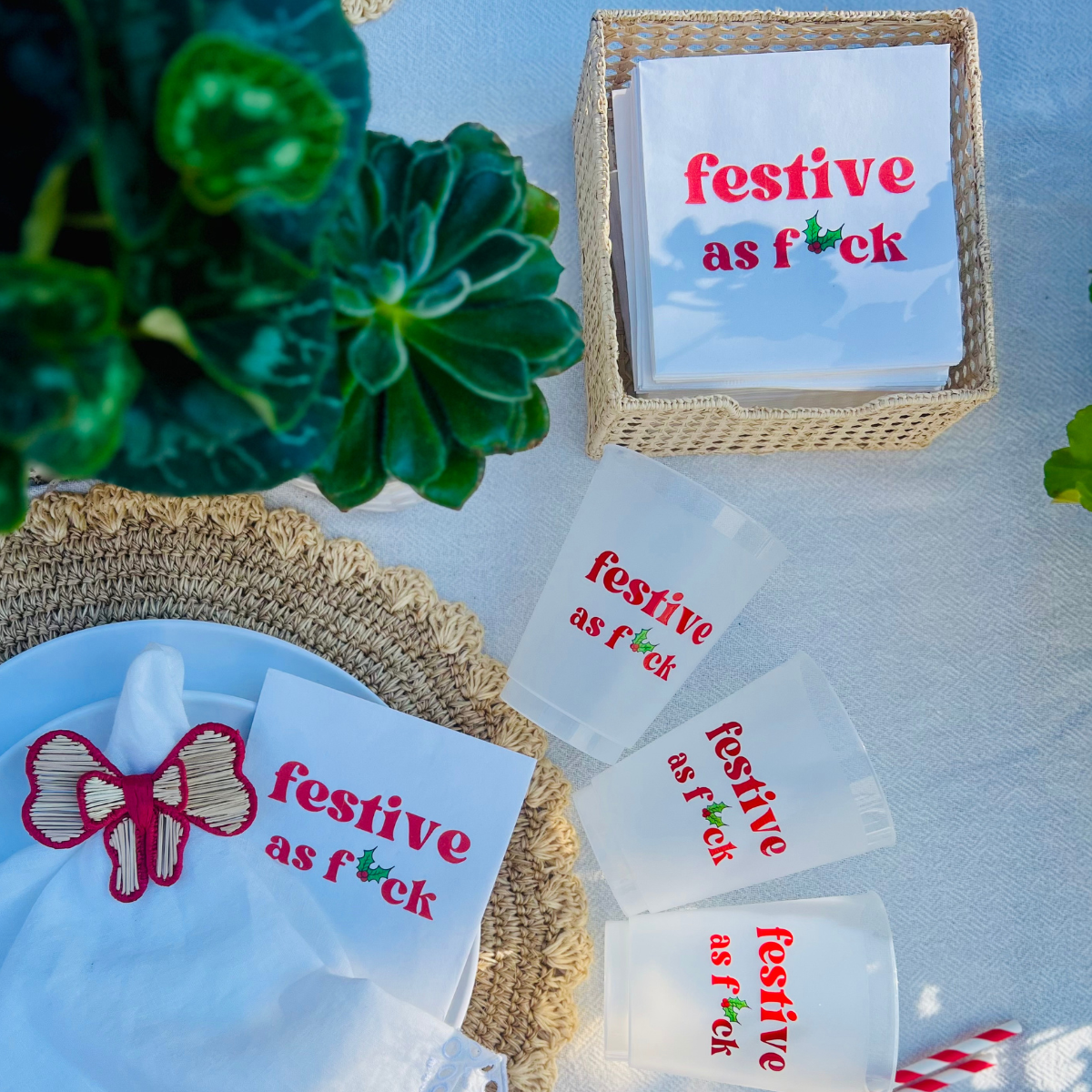 Festive-themed cocktail napkins and matching frost flex cups appear on a holiday table. The napkins and cups feature the text "festive as f*ck" in bold red font.  Perfect décor for naughty Christmas parties, Secret Santa Office gatherings, and holiday bars. 