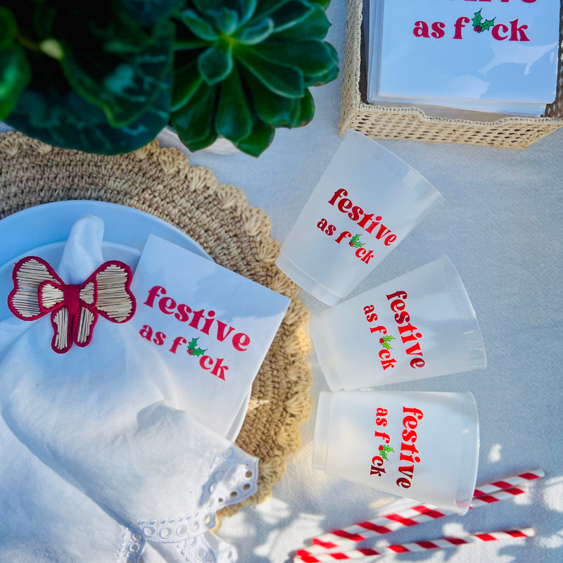 Clear frost flex cups with 'festive as f*ck' text on them are arced around a placemat with a plate that features a matching cocktail napkin. Perfect holiday décor for naughty Christmas parties. 