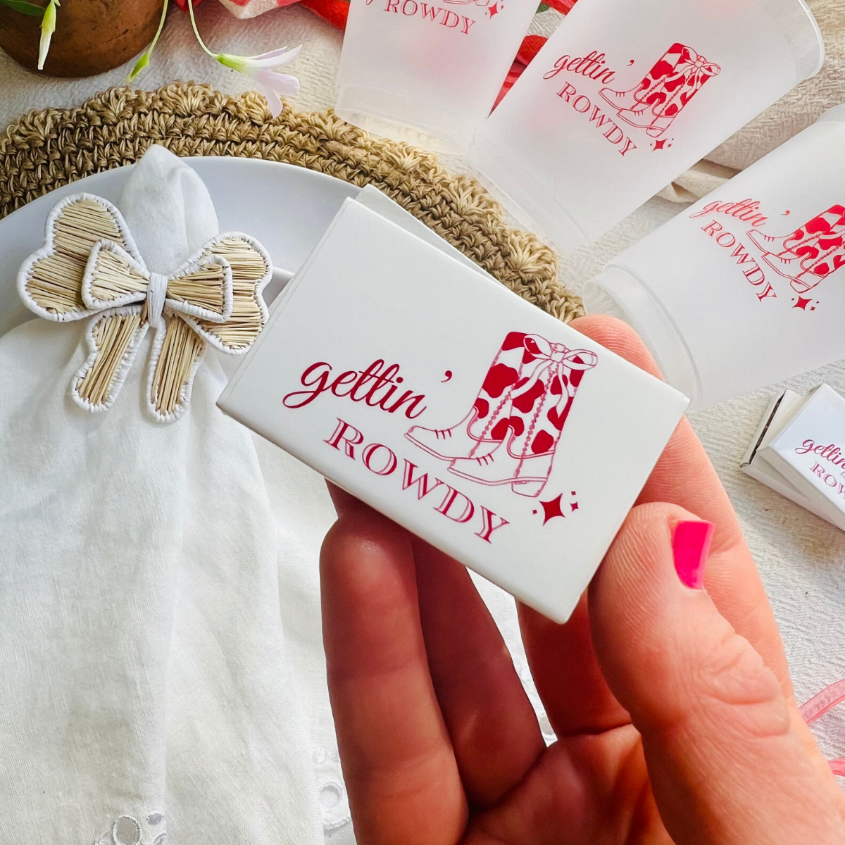 Hand holding a small white matchbox with 'gettin' Rowdy' branding, surrounded by matching "Gettin' Rowdy" frost flex cups.