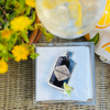 Hendrick's Gin napkin weight on a stack of white napkins on a table with flowers and a glass in the background