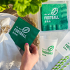 Green 'In My Football Era' napkins and cups on a white surface with a hand holding a napkin.