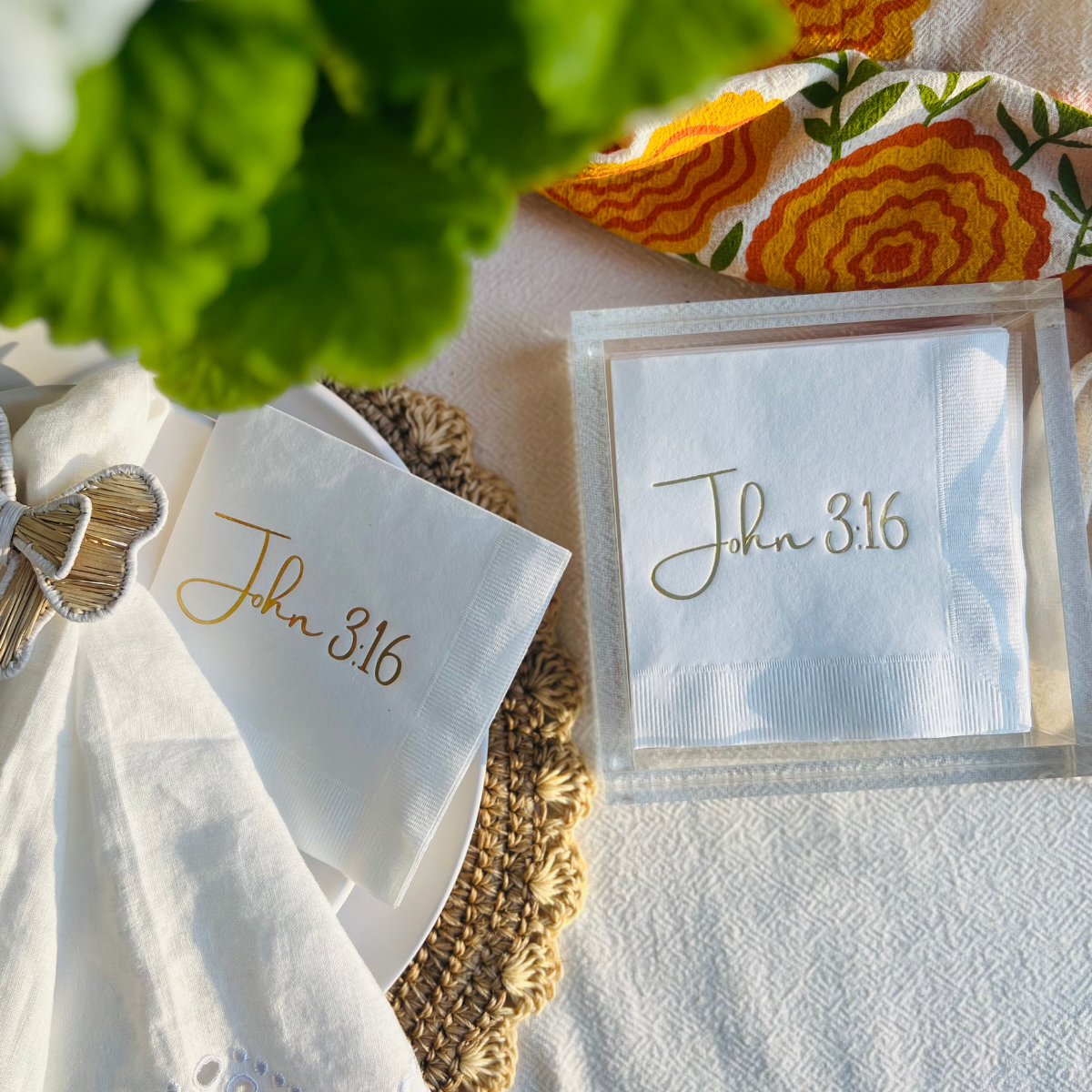 Napkins with 'John 3:16' printed on them, placed on a tablecloth with a decorative cloth in the background.