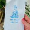 Hand holds up a white paper pindot guest towel with blue Buddha illustration and text that reads "Let That Shit Go"