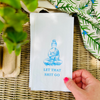 Hand holding a white paper guest towel with a blue Buddha illustration and text on a woven surface.
