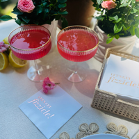 A white napkin featuring the saying "Let's Get Fizzicle" is styled on the table with cocktails.