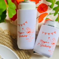 Two cans in white neoprene can coolers are shown from above on a textured table. The can coolers feature a matching design of an girl in a bikini in a martini glass for tini bit older themed birthday celebrations