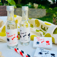 Two mini liquor bottles in a 'Mob Wives' theme show matching, customizable bottle labels and matching matchboxes with the same design are shown on a table in an outdoor setting