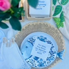 Decorative plate with blue floral design  is shown with a white cocktail napkin at its center. The text reads "New Baby New Home New Beginning" - a perfect closing or housewarming gift. 