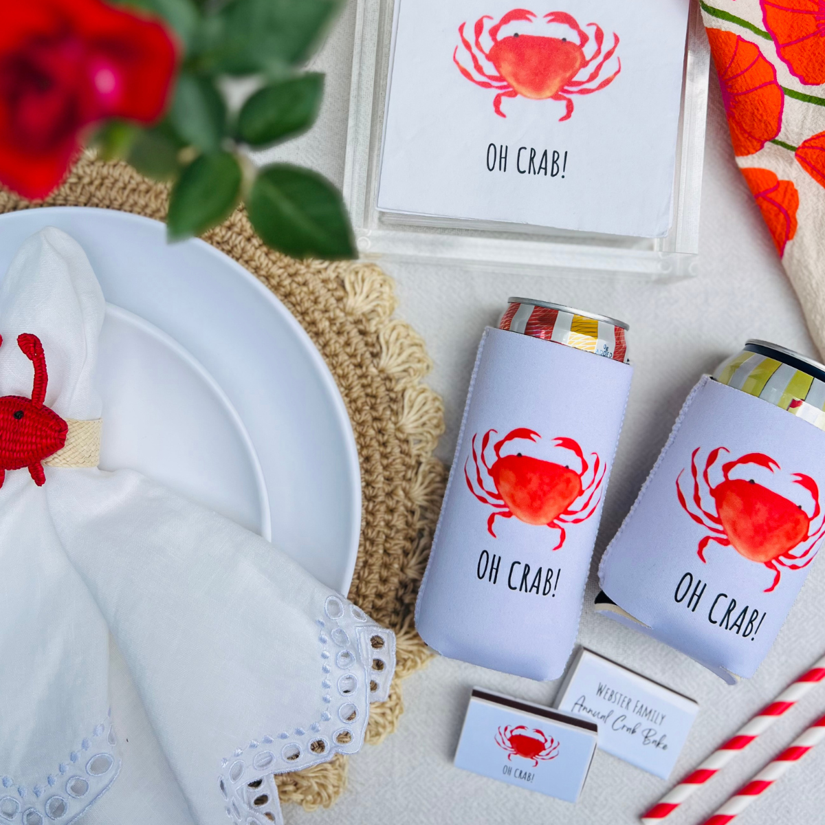 Cans with 'OH CRAB!' can coolers  on a table setting with napkins, matchboxes and straws.