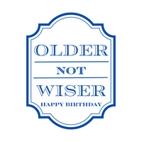 Close up of a white peel-and-stick wine label that features bold blue text that reads "Older Not Wiser - Happy Birthday."
