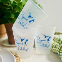Frosted cups with 'Pregnant Poolside' design on a table with plants and a plant pot in the background.