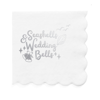 Decorative white paper cocktail napkin with 'Seashells & Wedding Bells' text and decorative elements in silver foil is shown on a white background.