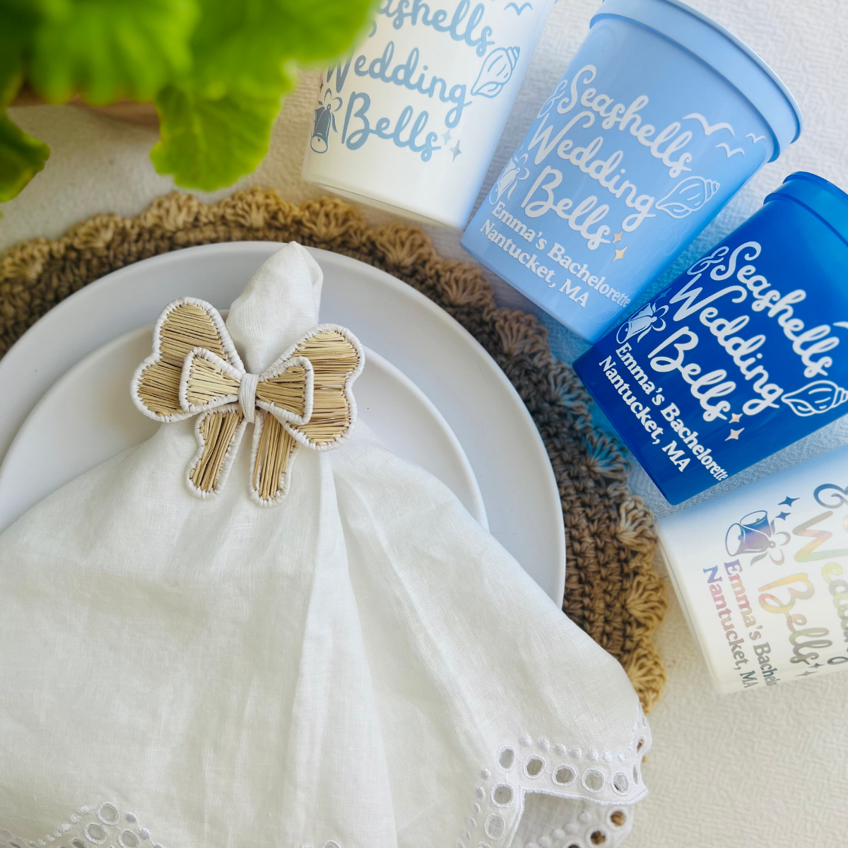 Napkin ring in the shape of a bow and 'Seashells Wedding Bells' customizable stadium cups on a table with decorative elements.  