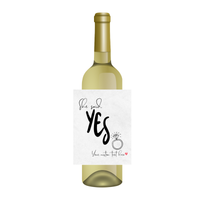 White wine bottle with a customizable engagement wine label that says 'She said Yes' on a white  background. Add the label to a bottle of wine or a champagne bottle for a novel engagement gift for the bride and groom-to-be.