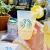 Hand holding a Shuck Yeah branded cup with lemon garnish outdoors.