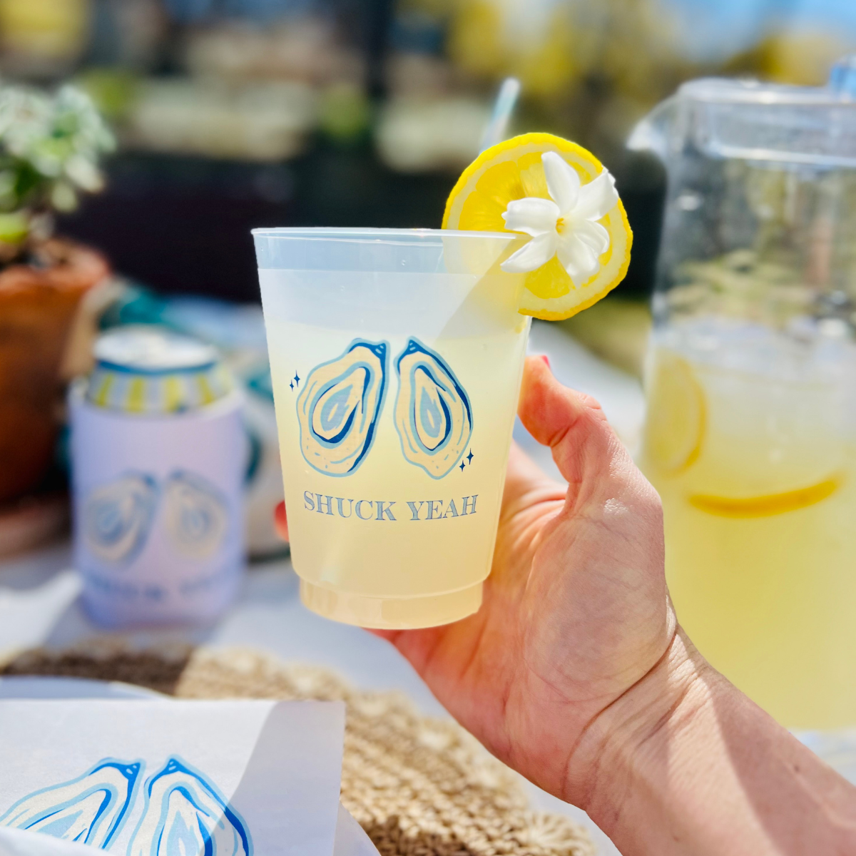 Hand holding a lemonade cup with 'Shuck Yeah' branding, outdoor setting
