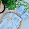 A cocktail napkin with matching can cooler sleeves features a design of shucked oyster shells and text that reads 'Shuck Yeah'
