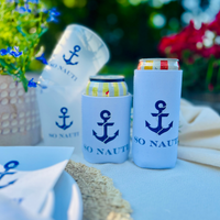 Can coolers with anchor design and 'SO NAUTI' text on a table with flowers and matching cups in the background