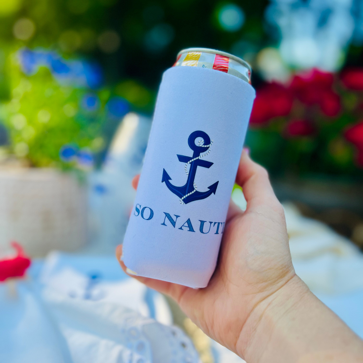 Hand holding a can with 'SO NAUTI' branding against a blurred outdoor background