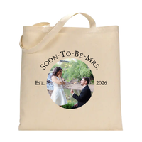 A natural canvas tote bag with two handles, featuring a circular printed photo of a couple and the text 'SOON-TO-BE-MRS.', 'EST. 2026