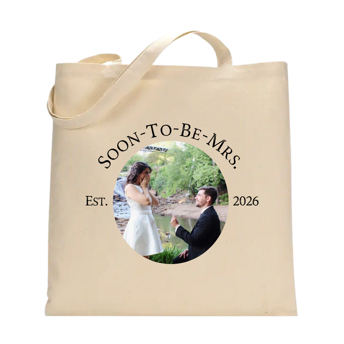 A natural canvas tote bag with two handles, featuring a circular printed photo of a couple and the text 'SOON-TO-BE-MRS.', 'EST. 2026