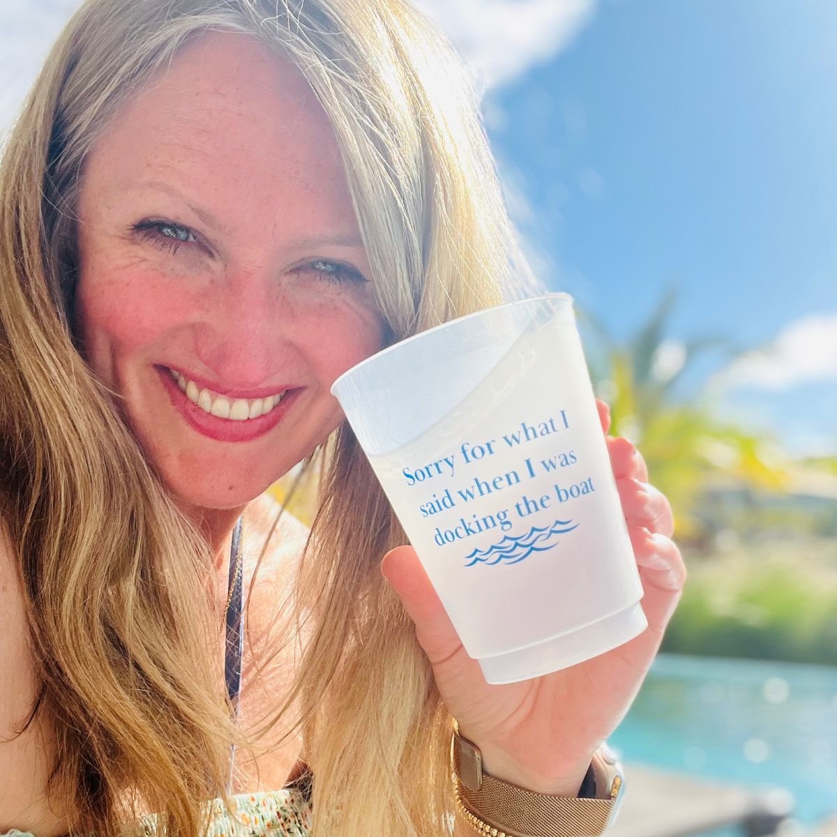 Woman holding a plastic cup with text that reads "Sorry for what I said when I was docking the boat" by a body of water