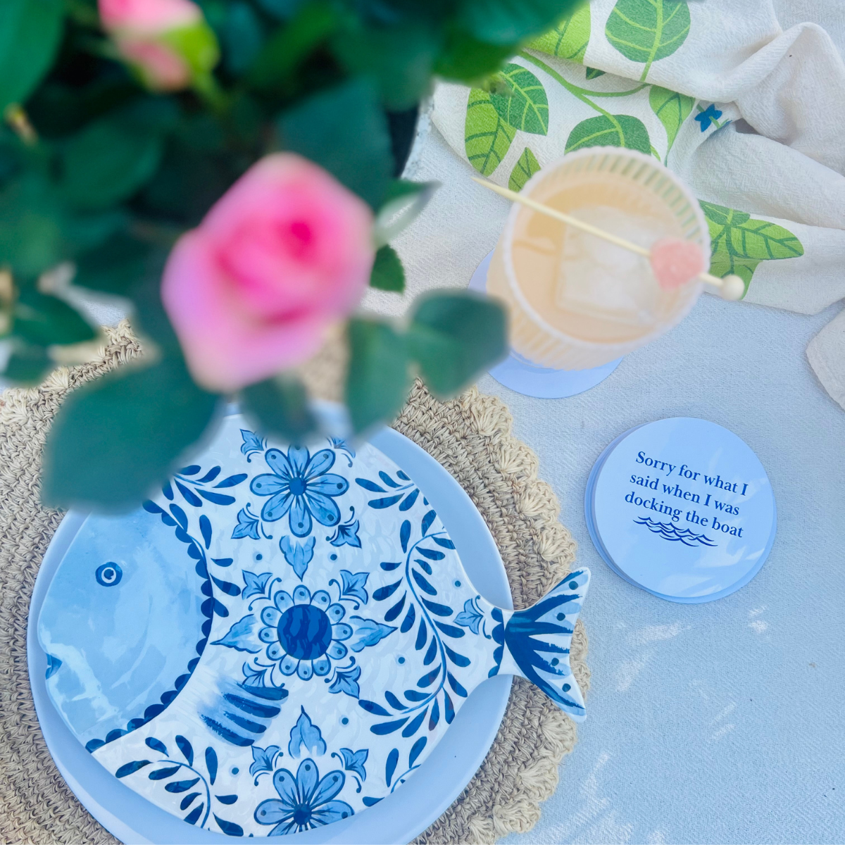 "Sorry for what I said when I was docking the boat" pulp board boating coasters are shown from above beside a plate in the shape of a fish and beside a cocktail glass. 