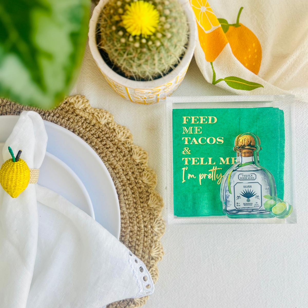 Tequila bottle acrylic napkin weight is shown on a green napkin with text 'Feed me tacos and tell me I'm pretty' on a table setting.