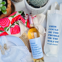Overhead shot of a wine bottle beside a matching canvas wine bag. Both the bottle and the wine bag feature the fun text "This Could Be The Problem Or The Solution - Let's find out." Perfect for gifting to a hostess, wine lover, or anyone who loves pairing wine with a good laugh. 