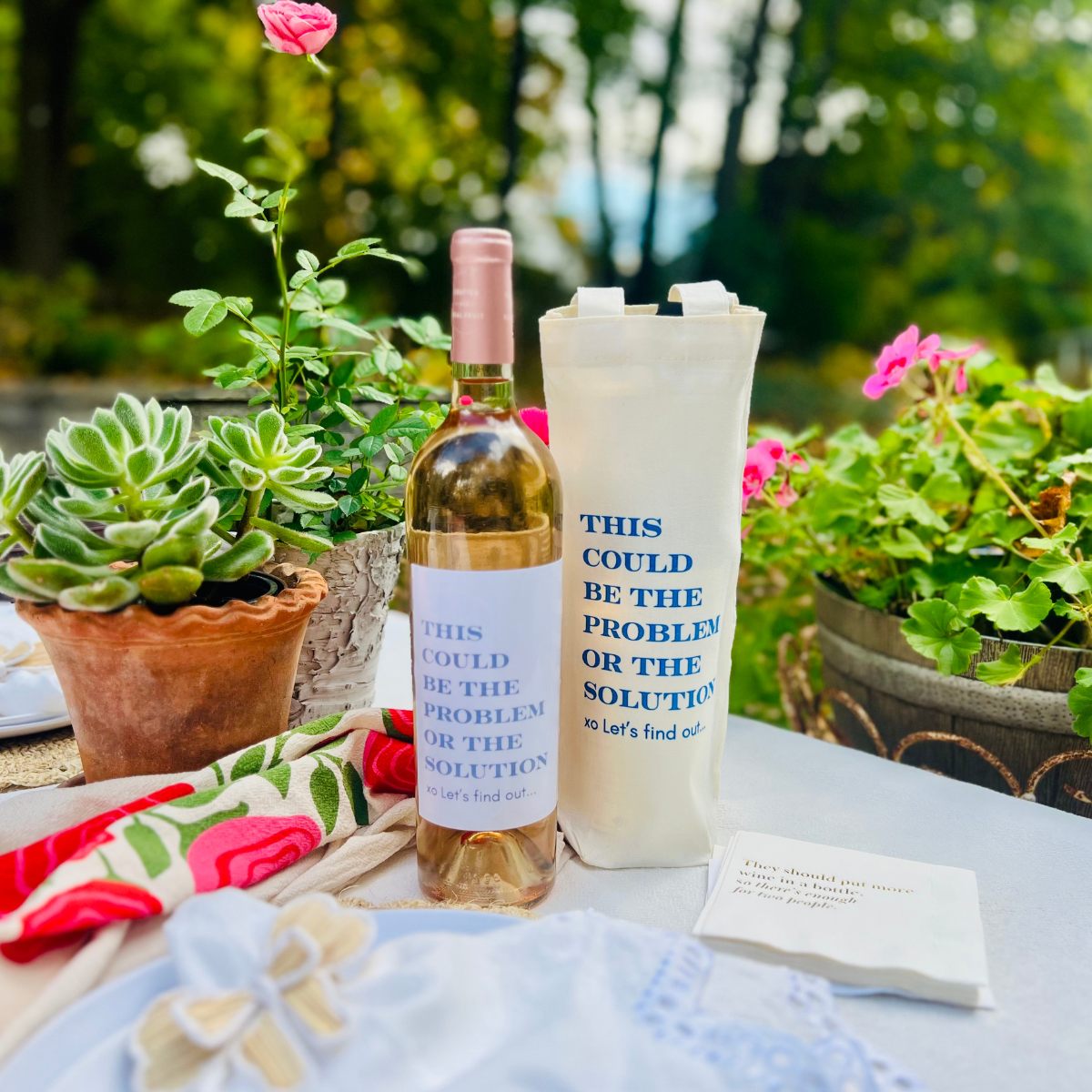 Wine bottle with a matching tote bag on a table outdoors with plants in the background