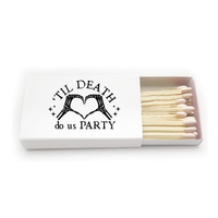 A novelty Halloween-inspired matchbox with black text that reads 'TIL DEATH do us PARTY' and a skeletal hand forming a heart shape. The open box contains light wood matches, and can be customized with up to 2 lines of text of the back.
