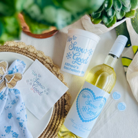 Bottle of white wine with 'Up to Snow Good' label, matching customized stadium bachelorette cups, and drink stirrers.