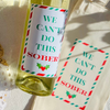 Bottle of wine with a humorous label on a light background is shown beside a matching canvas wine tote. Both the wine label and the tote feature a fun Christmas-themed design that says "We Can't Do This Sober" in green and red text within a festive green and red striped border. 