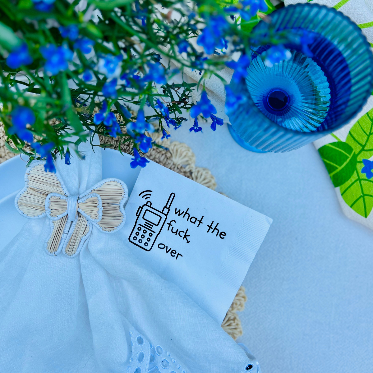 White cocktail napkin on plate with an illustration of a walkie talkie and text that reads "what the fuck, over"